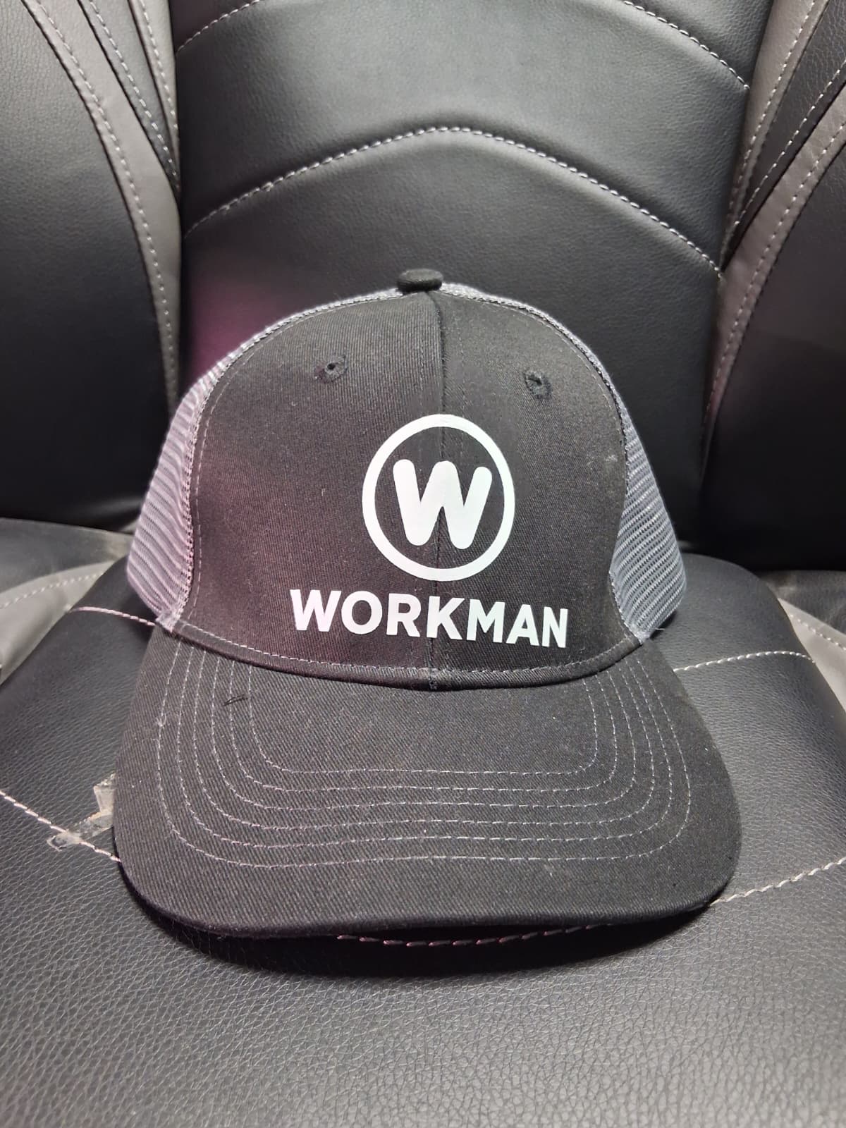A black hat with the WORKMAN circular W logo, sitting on a leather seat.